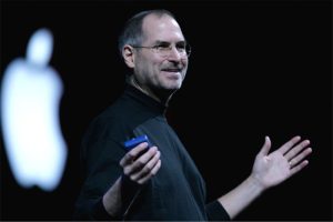 steve jobs creatorul apple in cadrul unei prezentari cu logo-ul in fundal